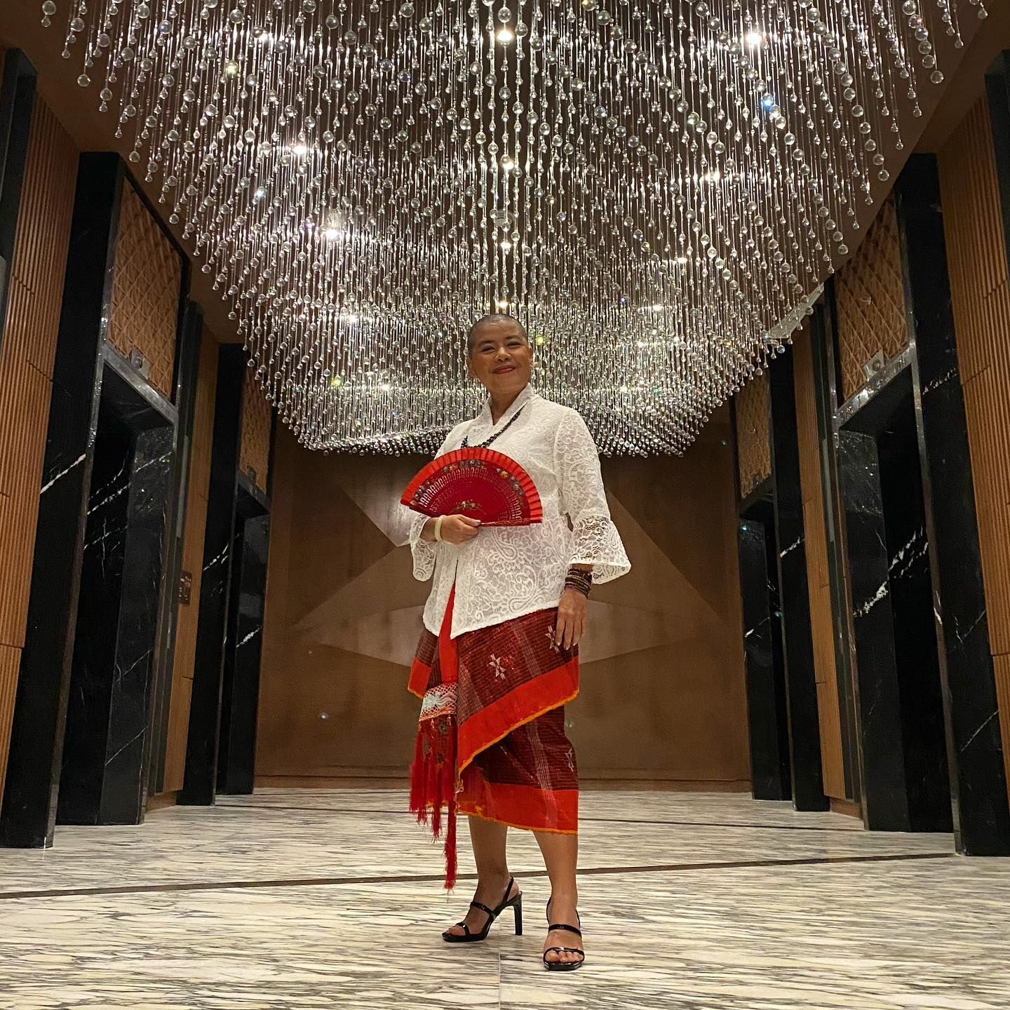 Terry Endropoetro kenakan kebaya dan kain tradisional Indonesia warna merah.