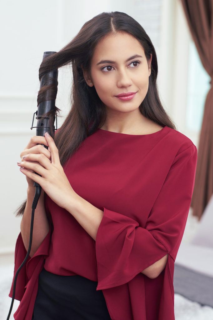 Pevita Pearce mengeriting rambut dengan curling wand menggunakan baju merah