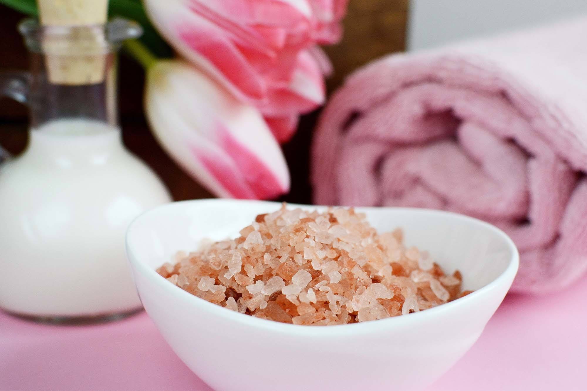 mangkuk garam himalaya berwarna pink dikelilingi handuk dan susu untuk membuat diy scrub kulit kepala