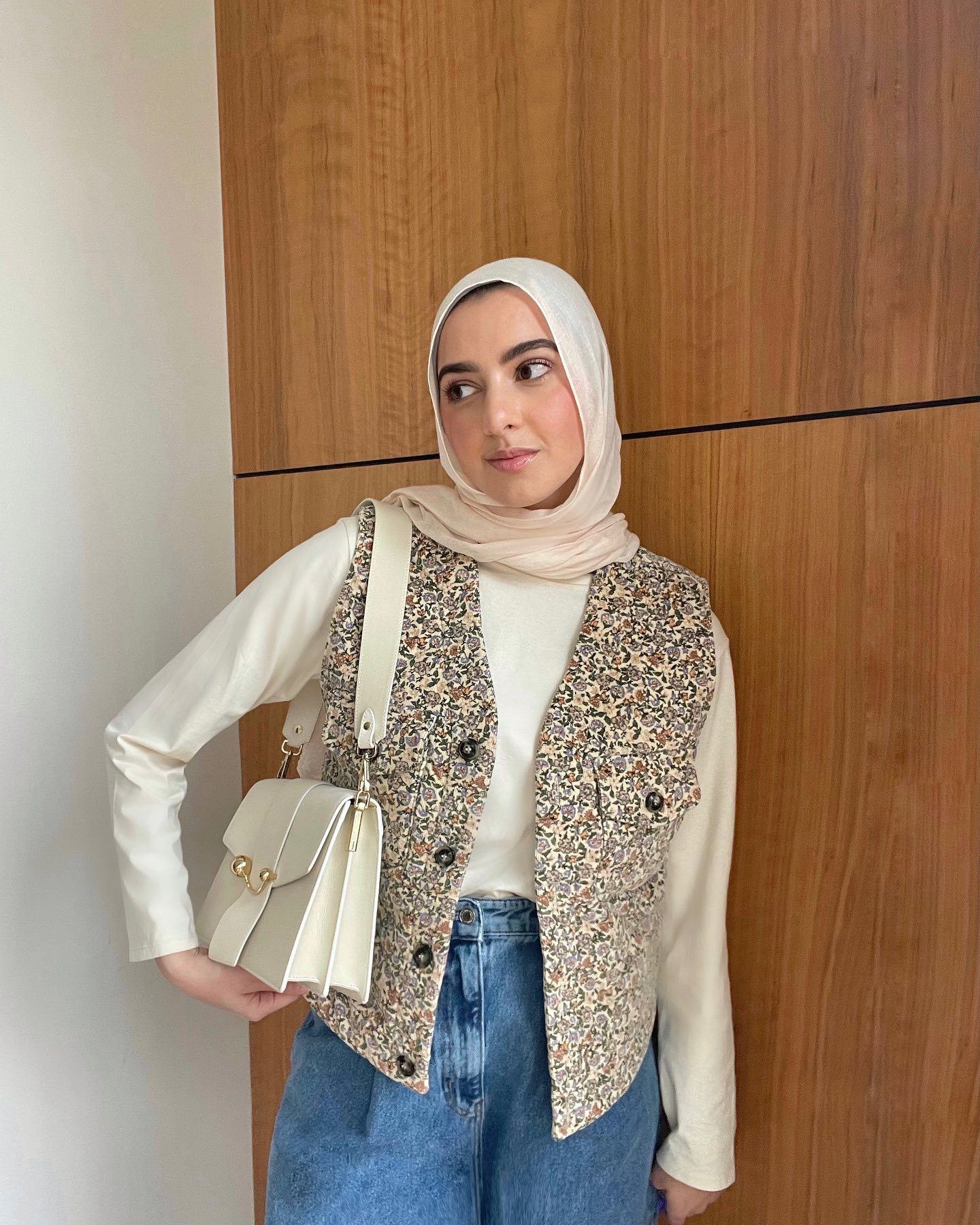 Wanita Kaukasia kenakan padanan outfit warna cream dari hijab dan baju serta vest motif floral.