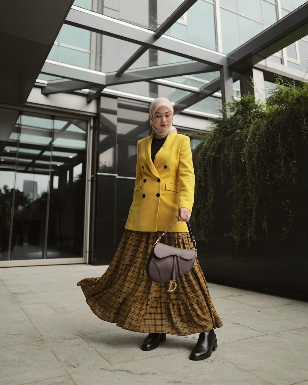 Indah Nada Puspita pakai blazer kuning, rok, dan sepatu boots berdiri di depan gedung