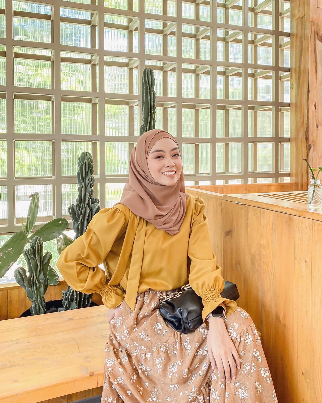 Richa Etika selebgram hijab duduk di kafe bernuansa kayu sambil tersenyum