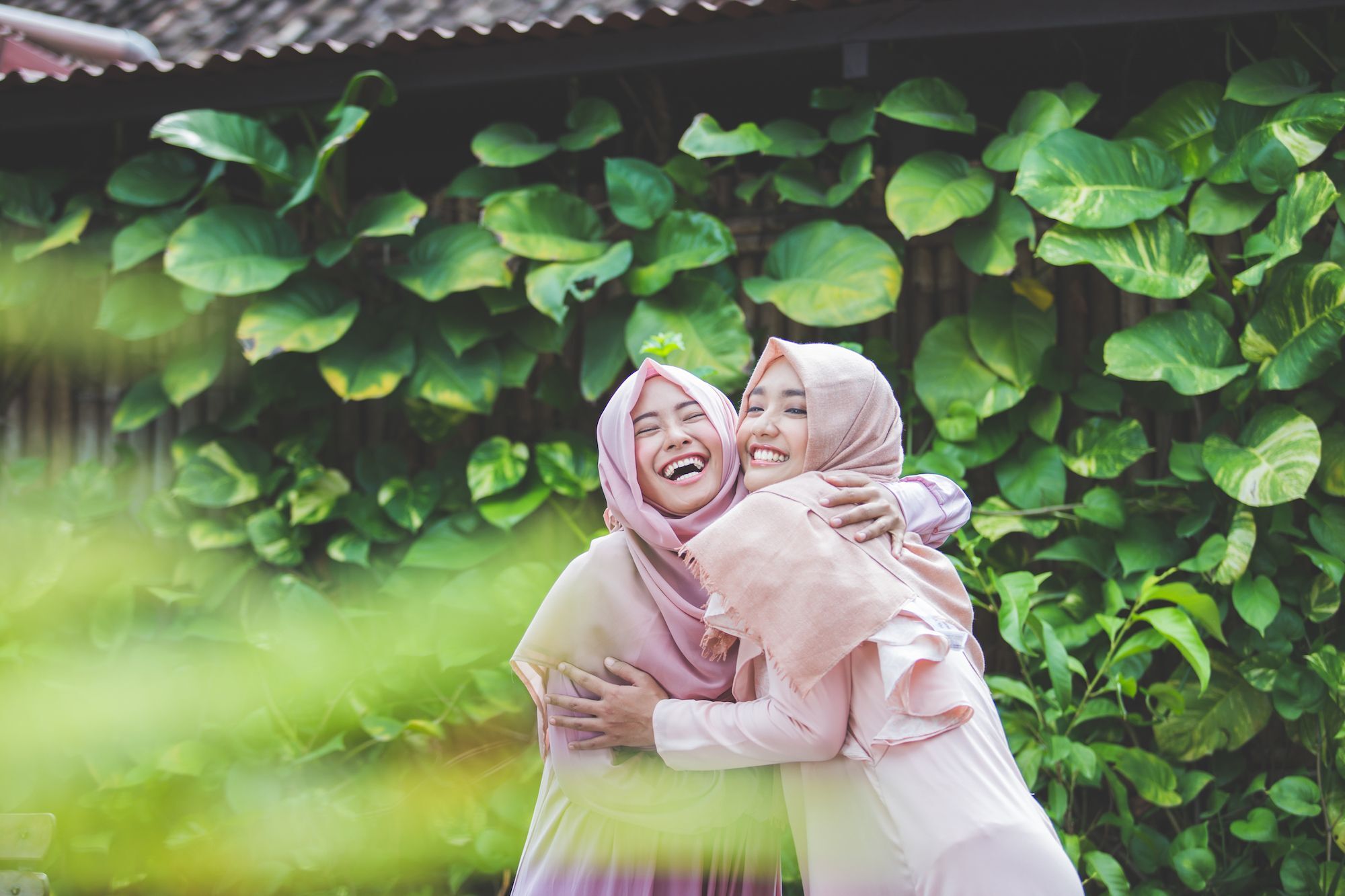 Dua wanita asia dengan hijab pink dan baju pink sedang berpelukan di taman