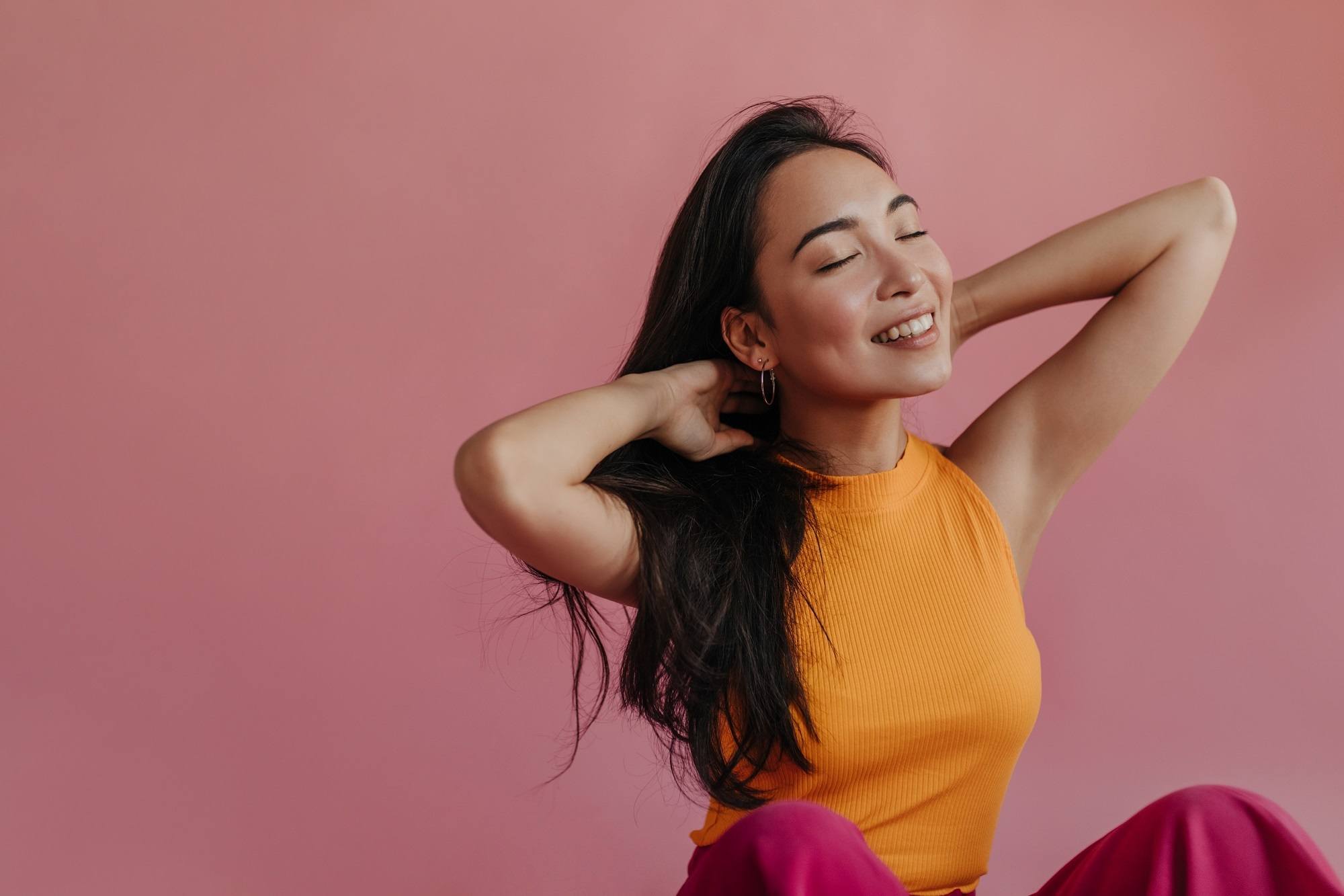 Wanita Asia pakai baju oranye sedang berpose duduk sambil memegang rambut panjang