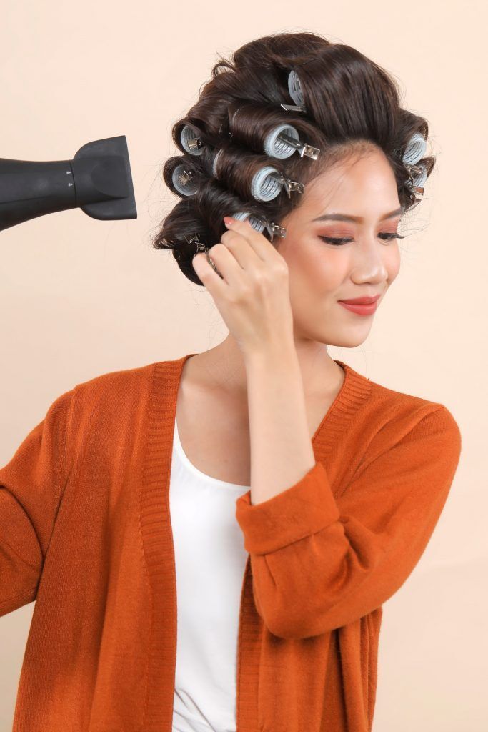 wanita asia menggunakan hairdryer pada rambut yang digulung menggunakan rol rambut