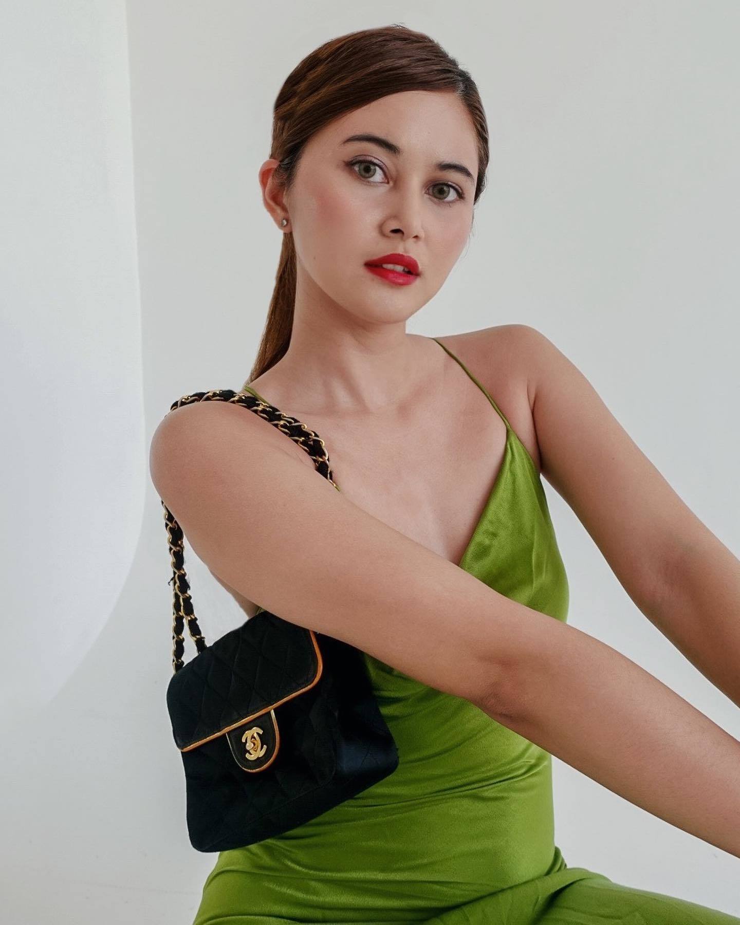 Wanita Indonesia berpose setengah duduk memakai dress hijau dengan makeup yang bold.