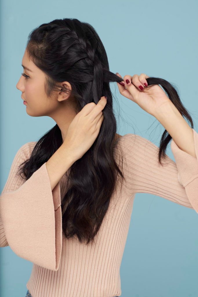 Wanita asia dengan rambut panjang warna hitam menggunakan baju pink sedang mengepang rambut