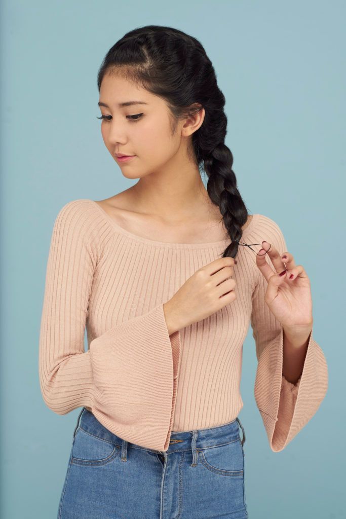 Wanita asia dengan warna rambut hitam menggunakan baju pink sedang mengikat kepang rambut