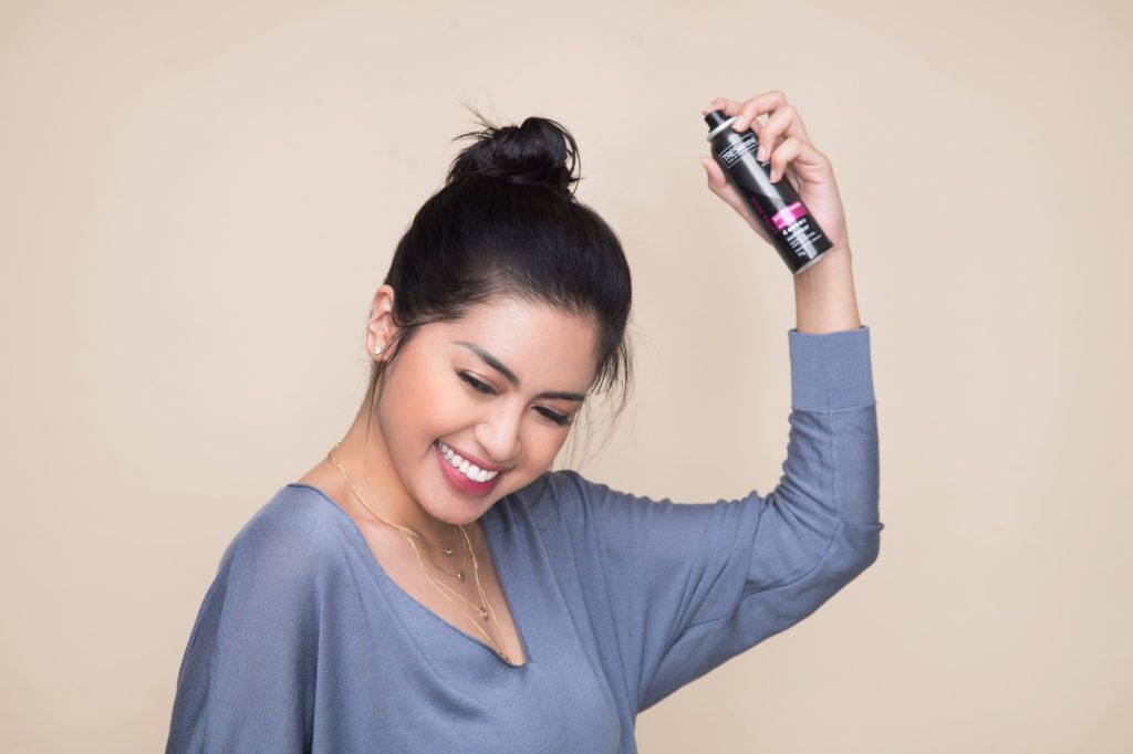 Wanita asia dengan rambut hitam sedang menyemprotkan hair spray