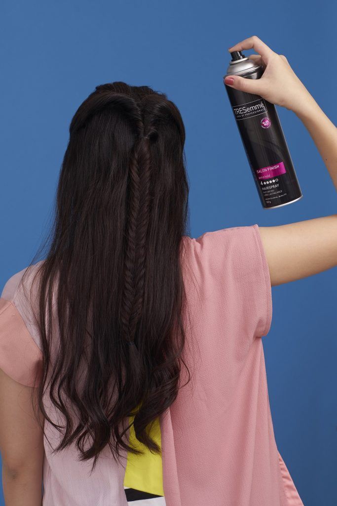 Wanita Asia sedang menyemprot hairspray pada model rambut twisted fishtail braid