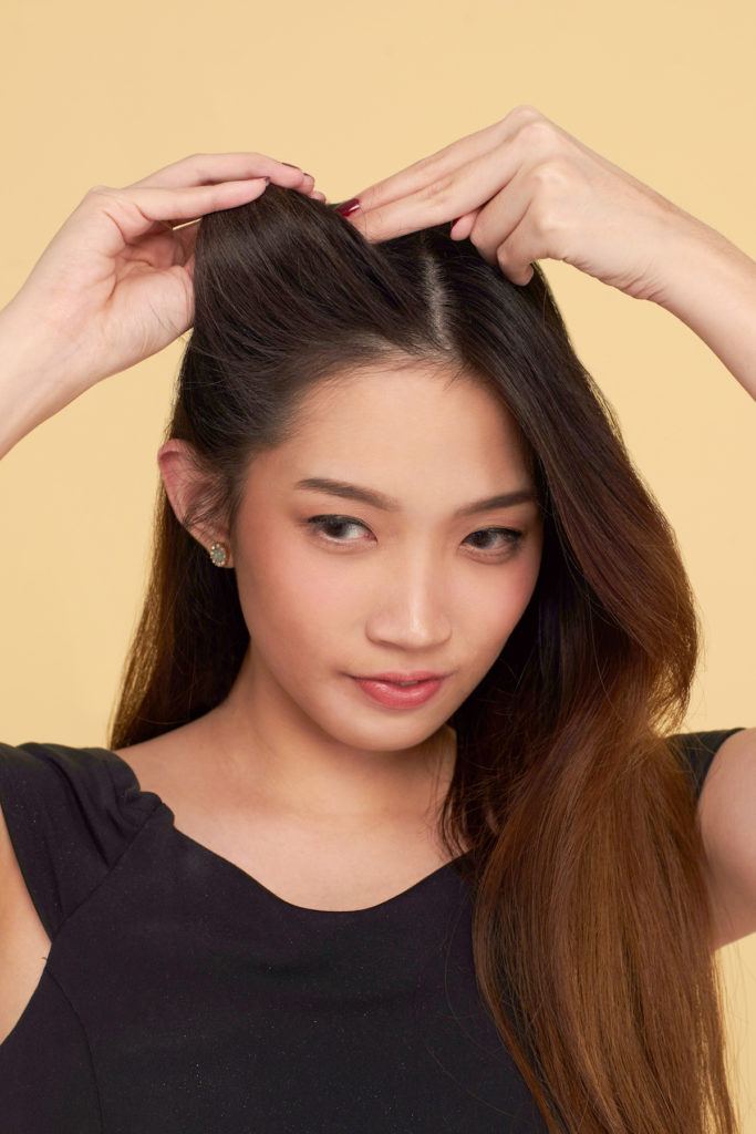 Wanita asia dengan rambut panjang sedang menata rambut dengan jari.