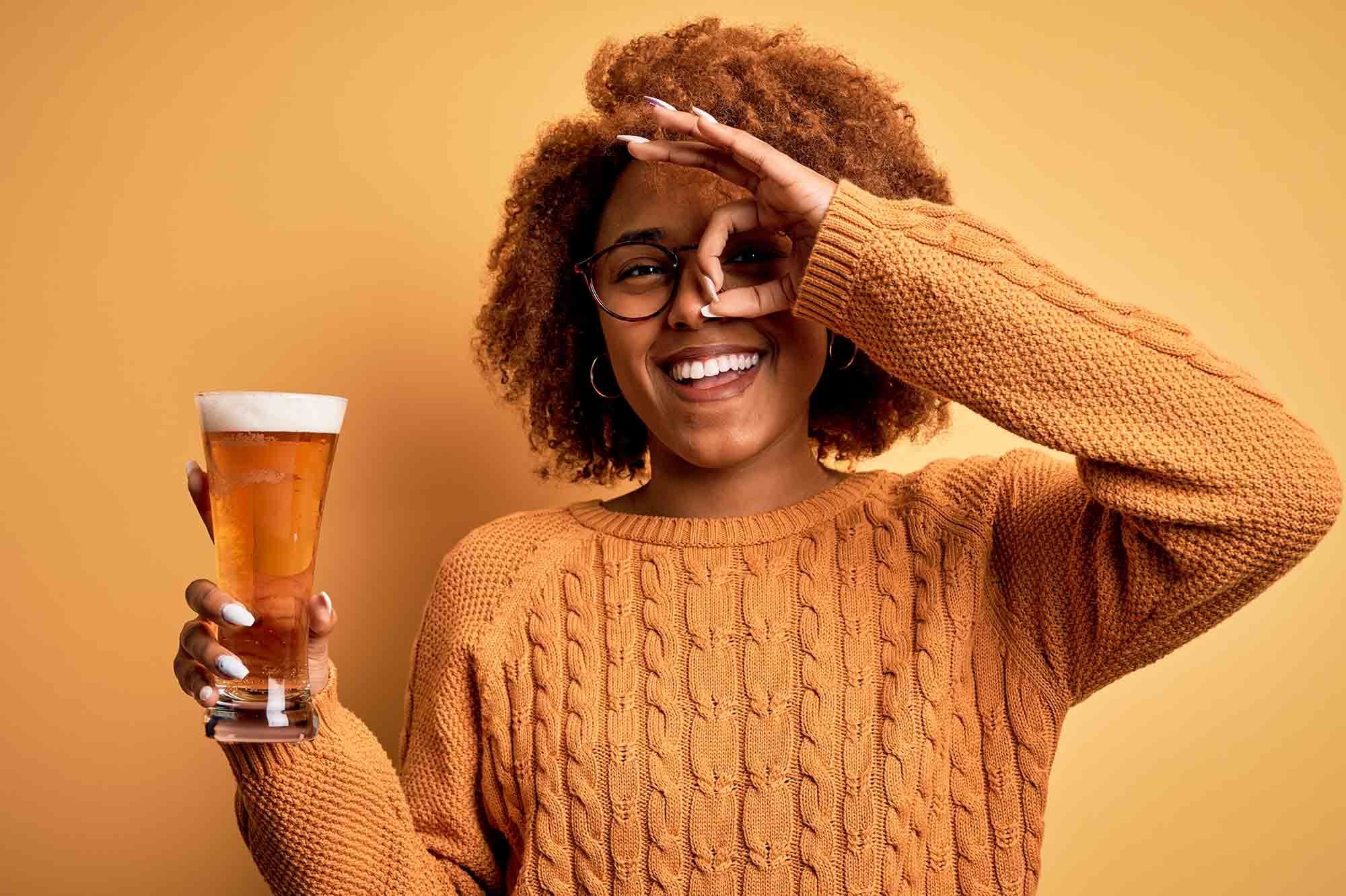 wanita berkulit gelap dan berambut keriting dengan sedang memegang gelas bir