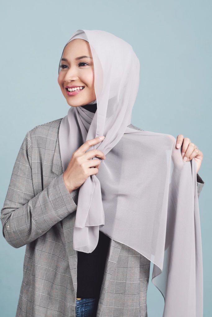 Wanita asia menata hijabnya dengan disilang