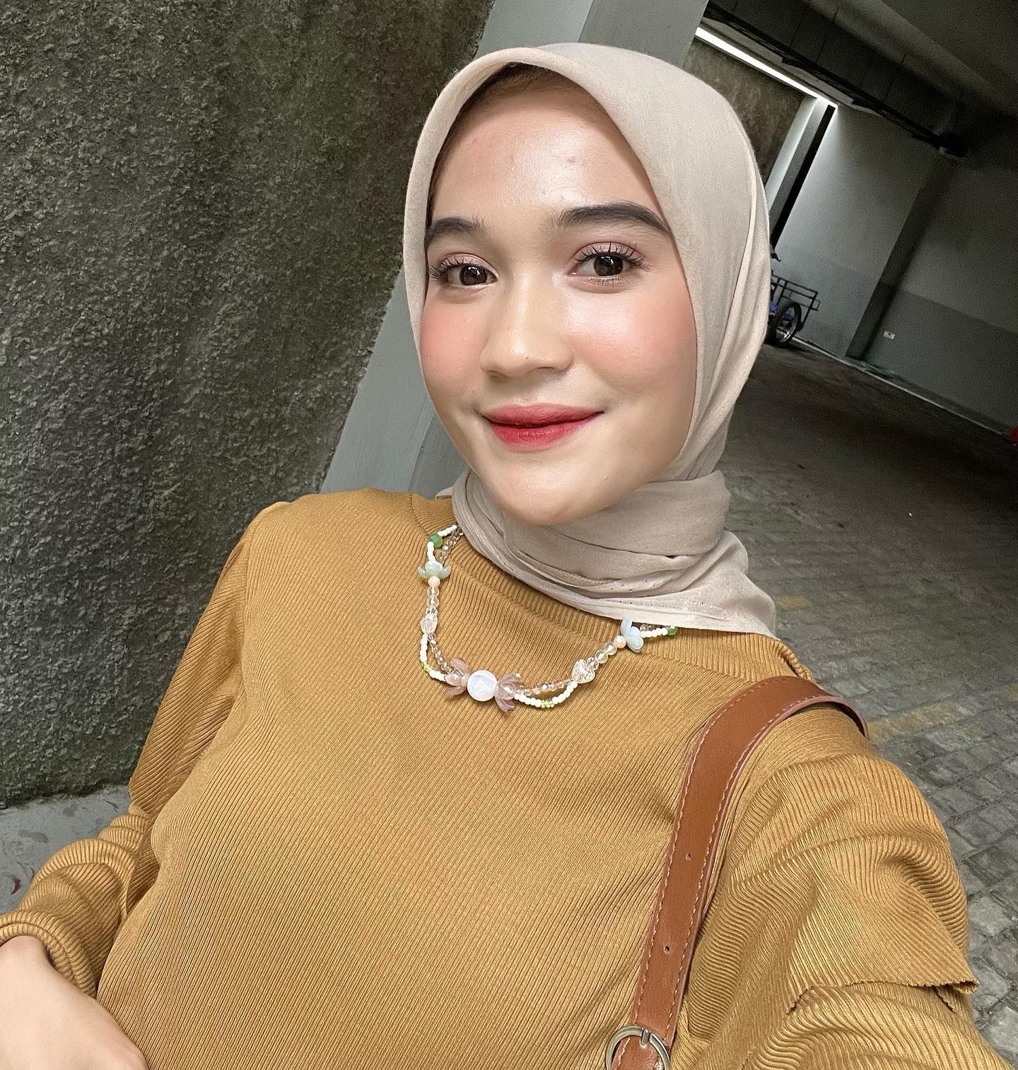 Wanita Asia memakai hijab segiempat warna nude dengan kalung manik-manik berwarna senada.