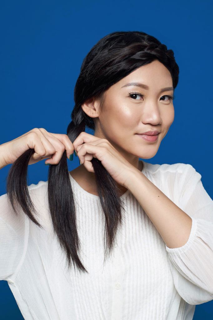 Wanita asia dengan rambut hitam panjang menata rambut gaya crown braid.