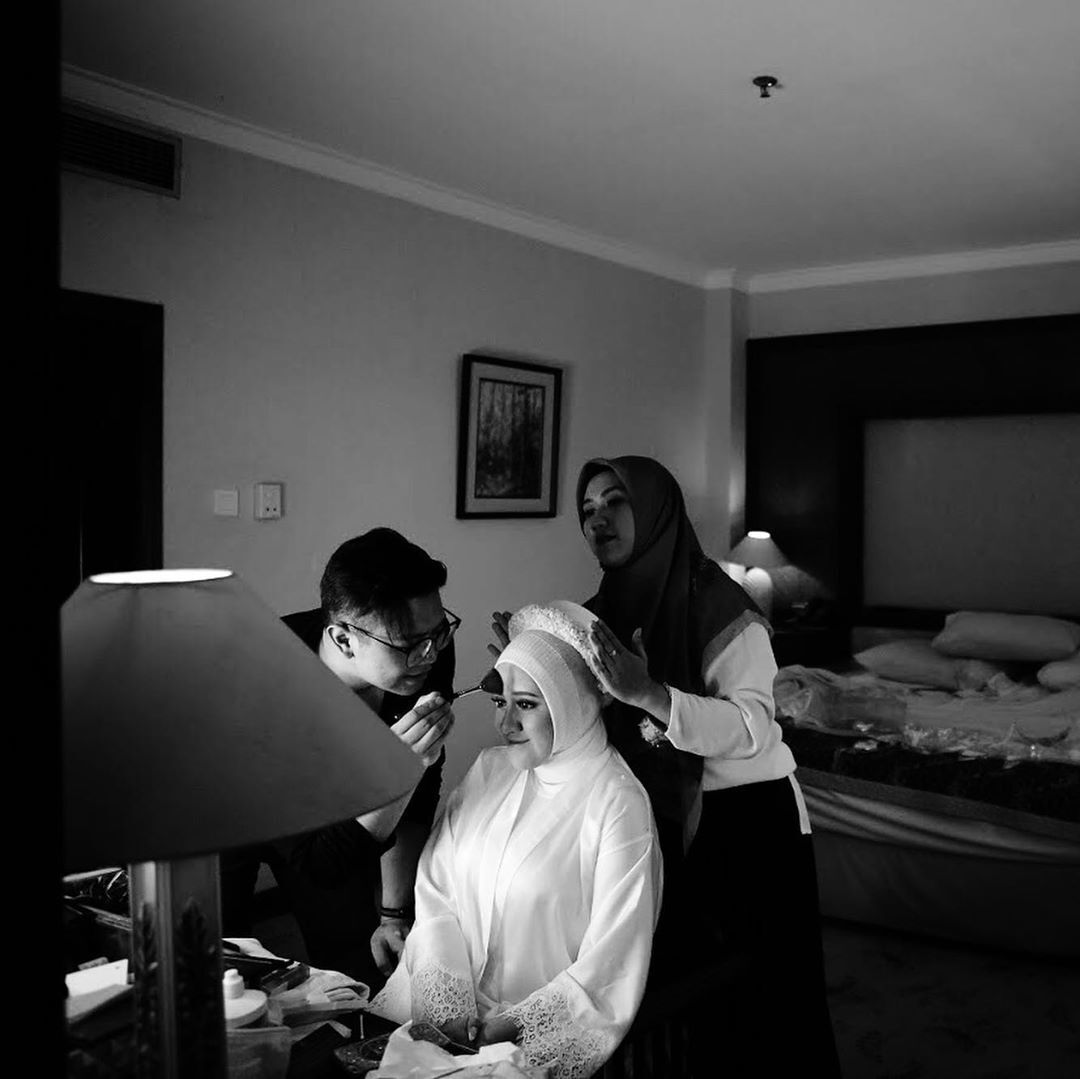 Hijab stylist sedang merapikan hijab pengantin wanita di kamar hotel
