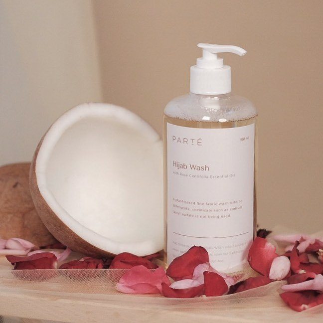 Deterjen khusus hijab dalam botol dengan kelapa dan kelopak mawar mengitarinya.