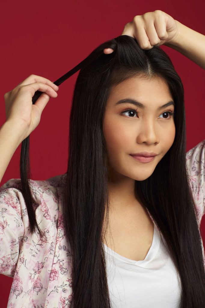 Wanita asia dengan rambut hitam panjang membuat twist pertama pada rambut bagian atas - double french twist ponytail