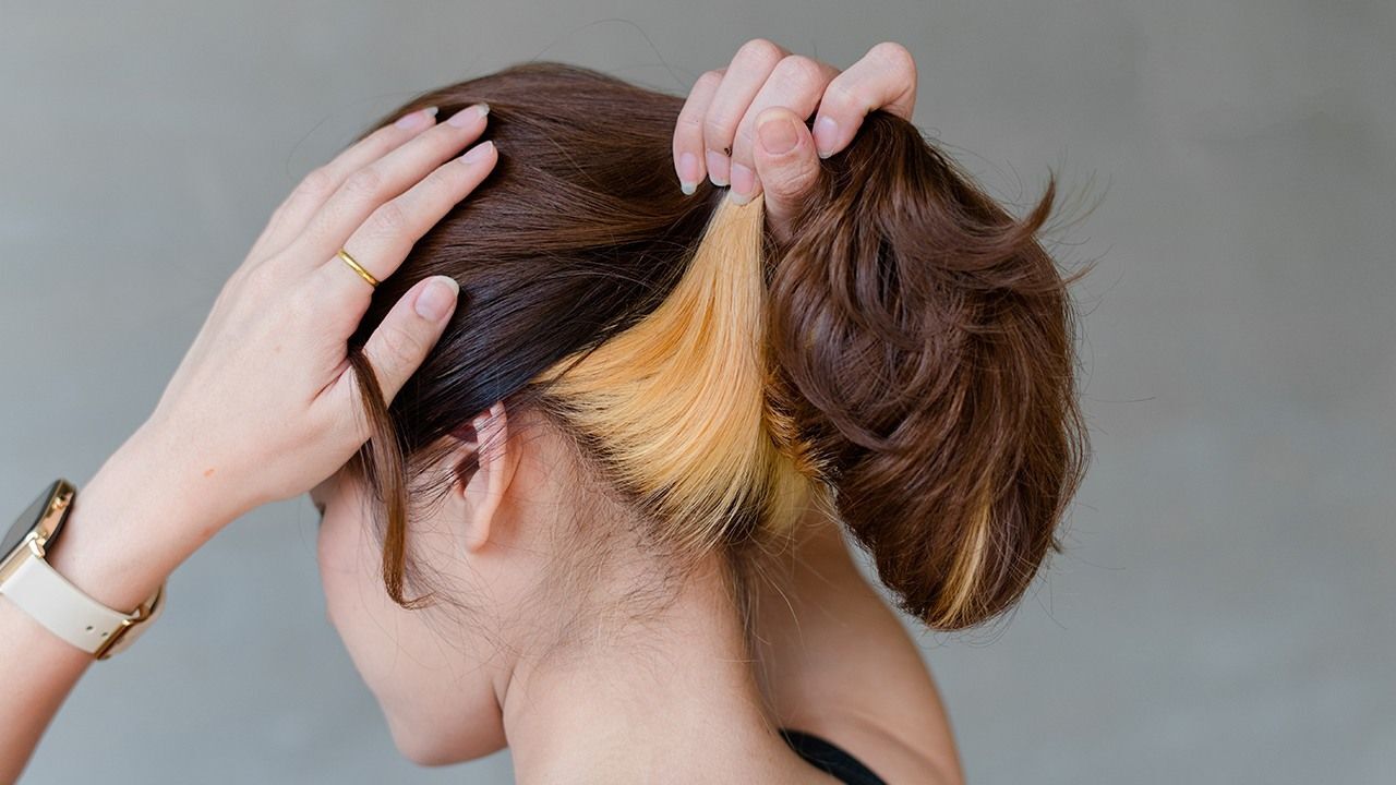 wanita asia sedang mengangkat rambut dan menunjukkan rambut warna peekaboo pirang