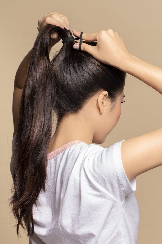 wanita asia sedang mengikat ponytail untuk membuat messy fan bun