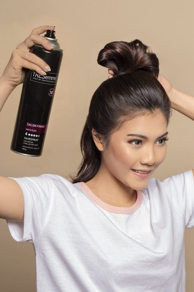 Wanita asia menyemprokan hairspray pada cepol rambut