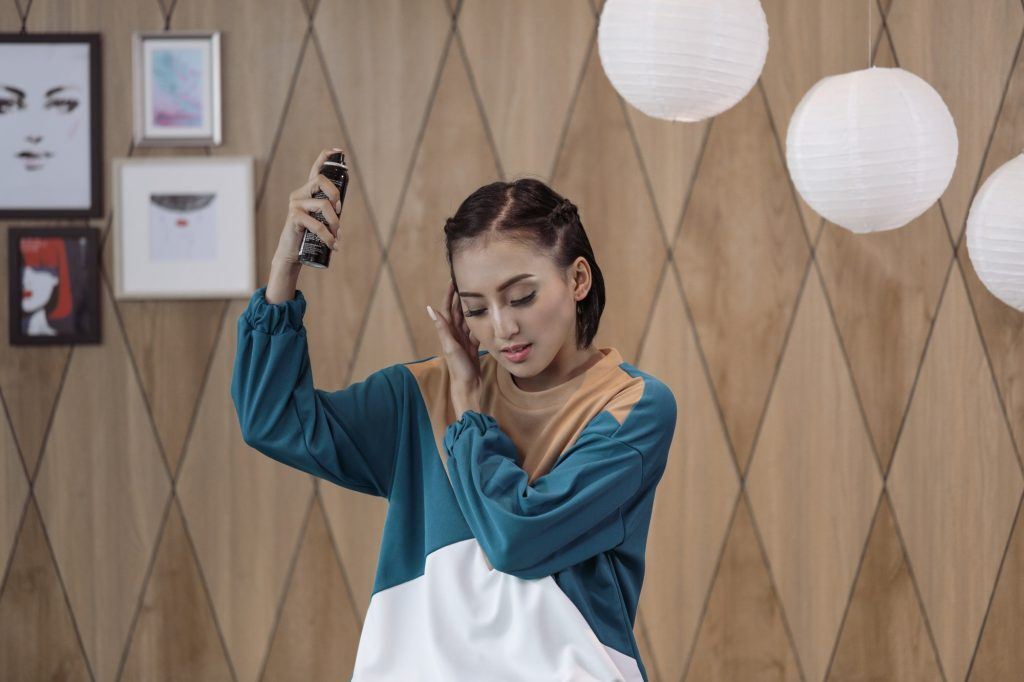 Wanita Asia dengan kepang samping menyemprotkan hairspray