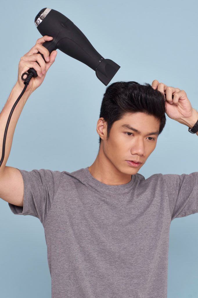 Pria asia dengan rambut hitam menata gaya quiff dengan menggunakan hairdryer
