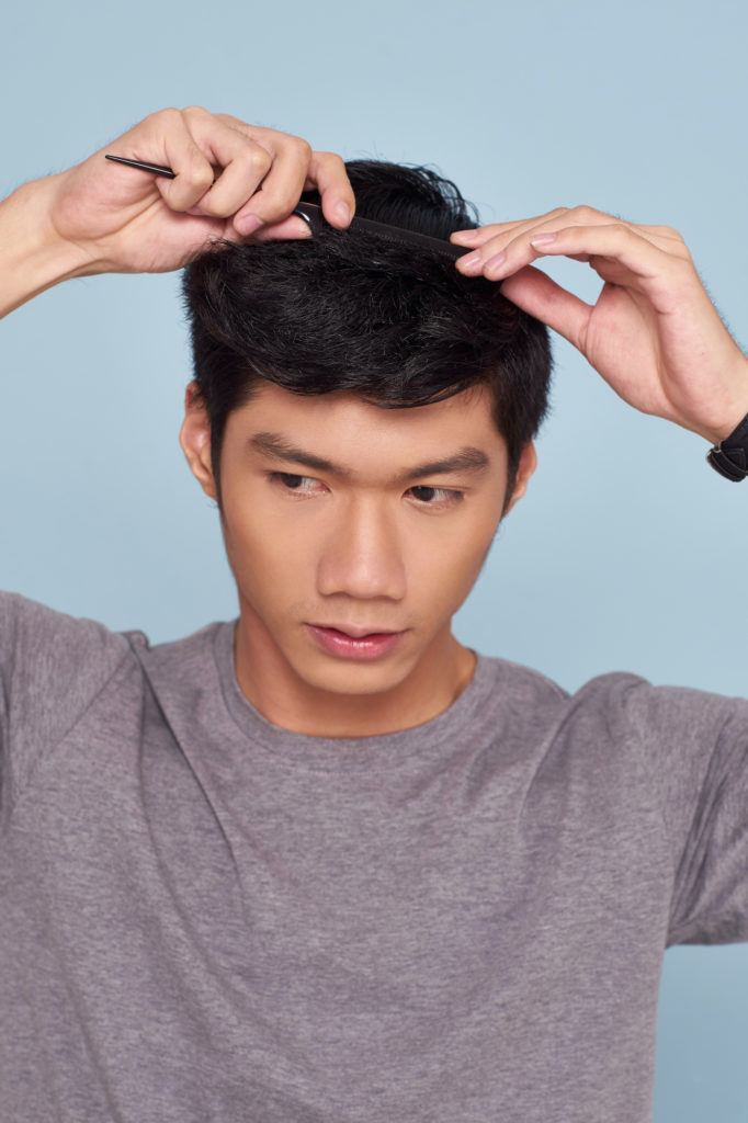 Pria asia dengan warna rambut hitam menata rambut gaya quiff dengan sisir.