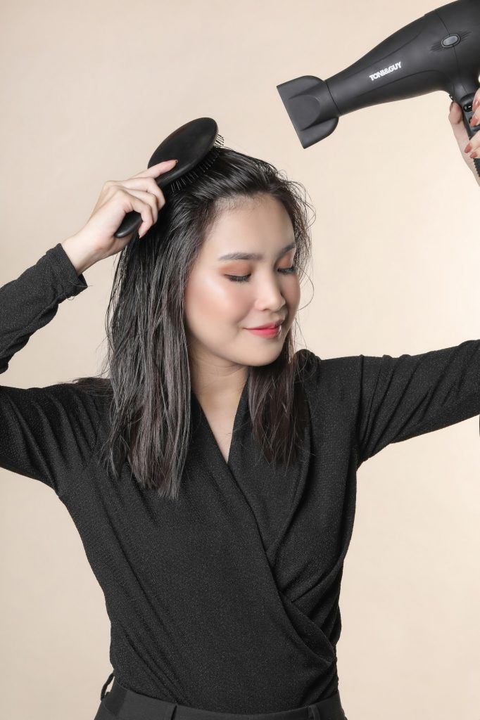 wanita asia sedang menyisir dan mengeringkan rambut dengan hairdryer