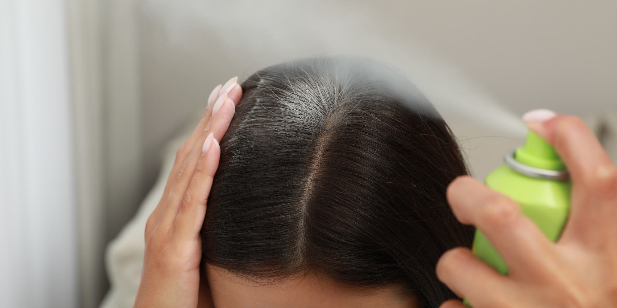 wanita sedang meggunakan dry shampoo dalam bentuk spray ke kulit kepala