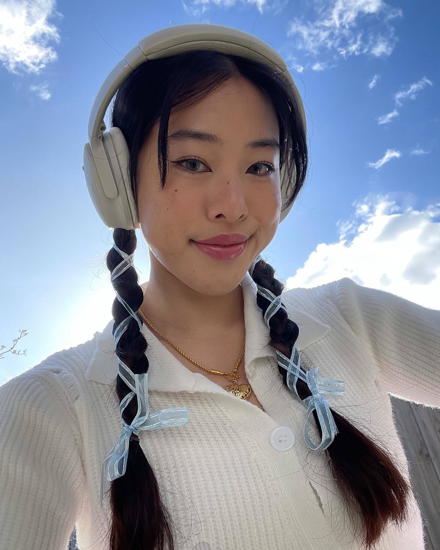 Wanita Asia dengan gaya rambut kepang dua memakai headphone warna putih.
