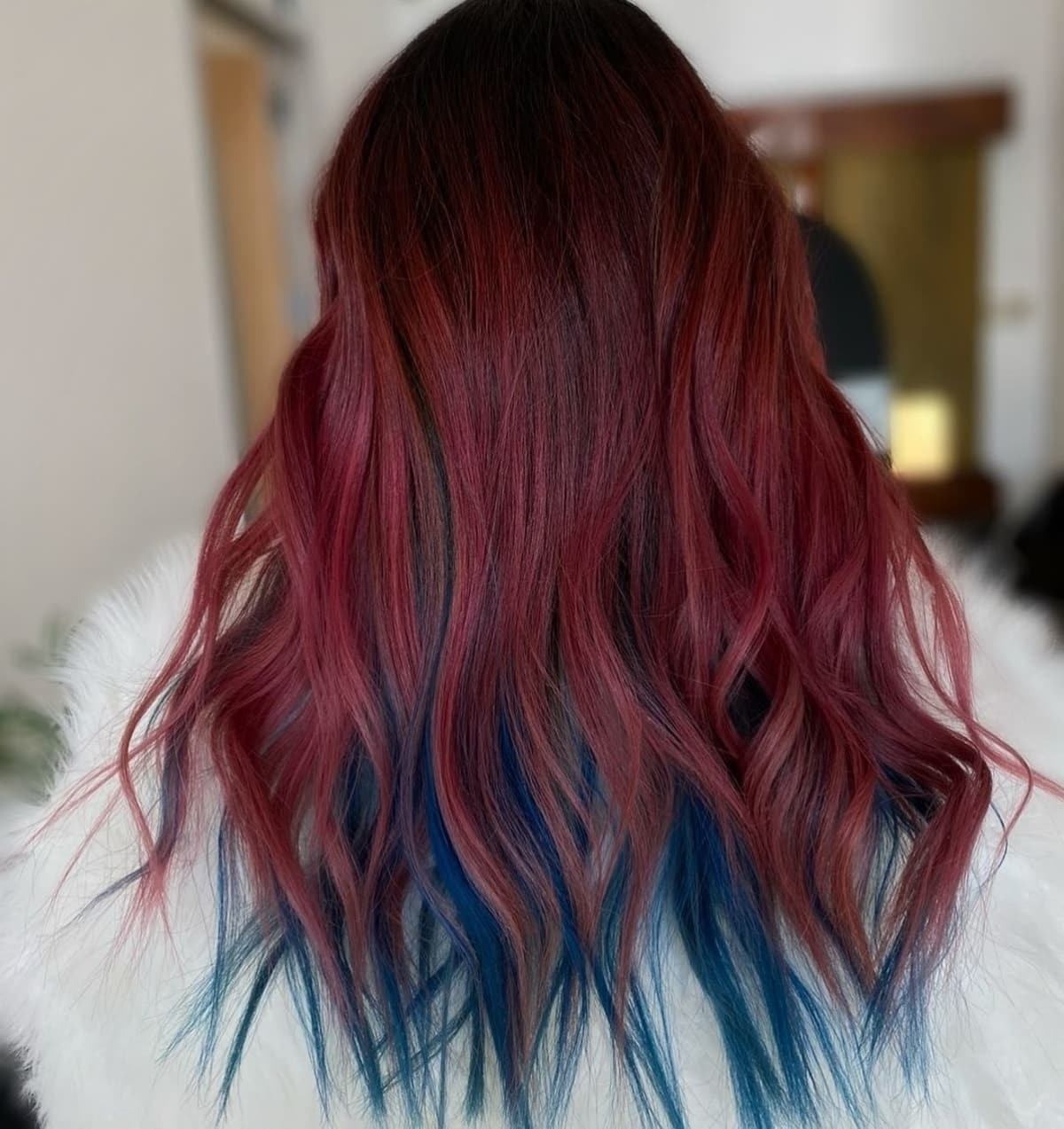 wanita dengan rambut panjang bergelombang warna merah maroon dan peekaboo hair biru