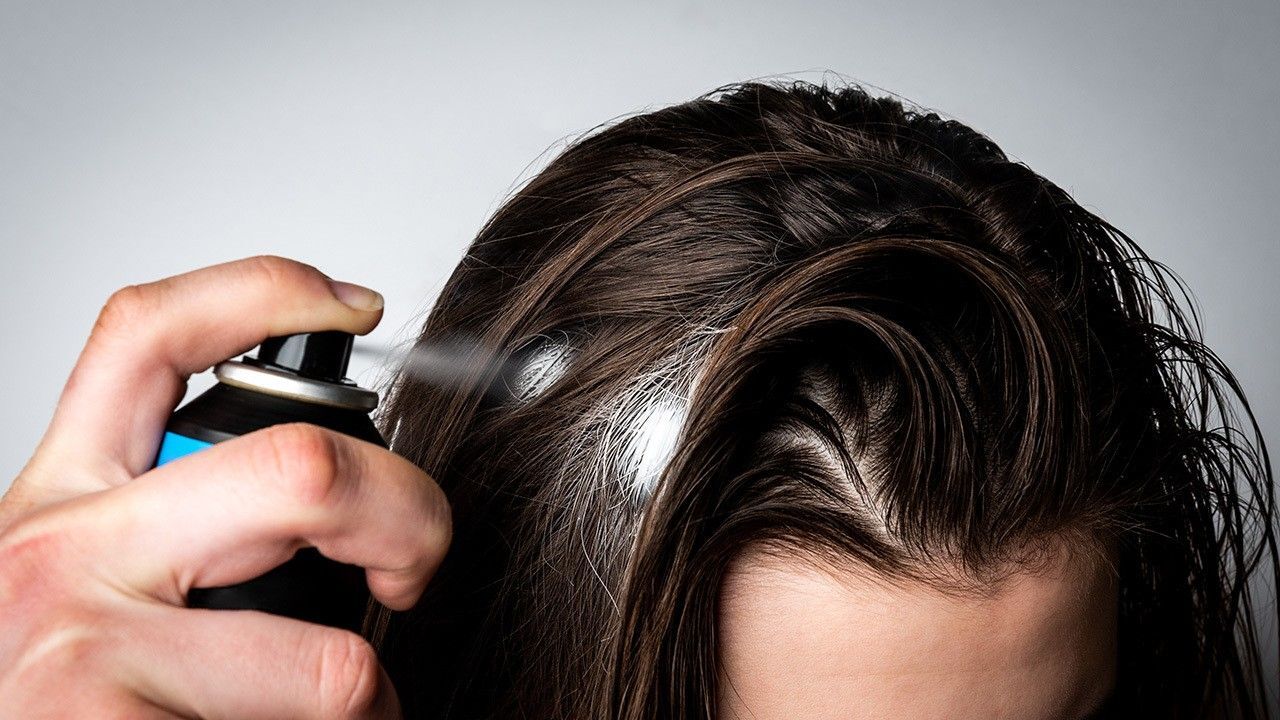 wanita sedang menyemprotkan dry shampoo dan meninggalkan serbuk putih