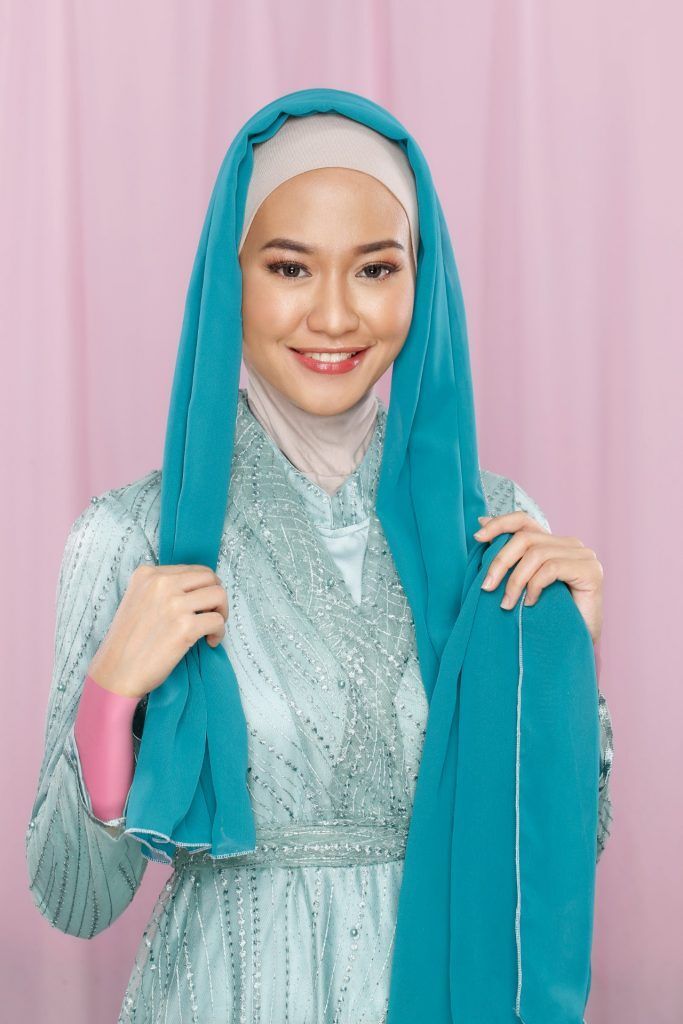 Wanita memasangkan hijab pashmina hijau di kepalanya