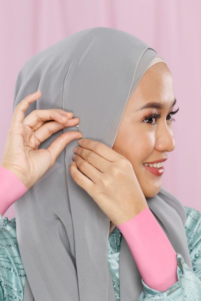 Wanita menyematkan jarum pentul di samping hijabnya.