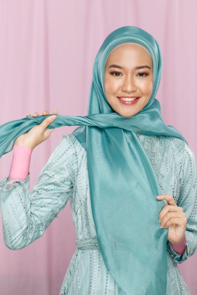 Wanita menunjukkan tutorial hijab pesta memakai jilbab organza.