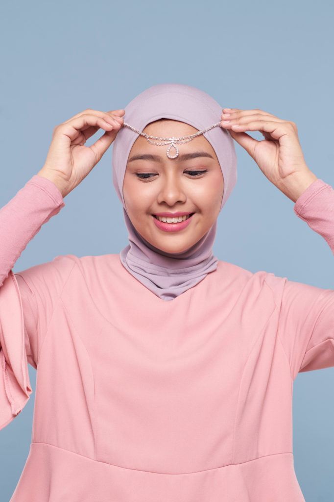 Wanita asia menggunakan ciput meletakkan aksesori pada hijabnya.