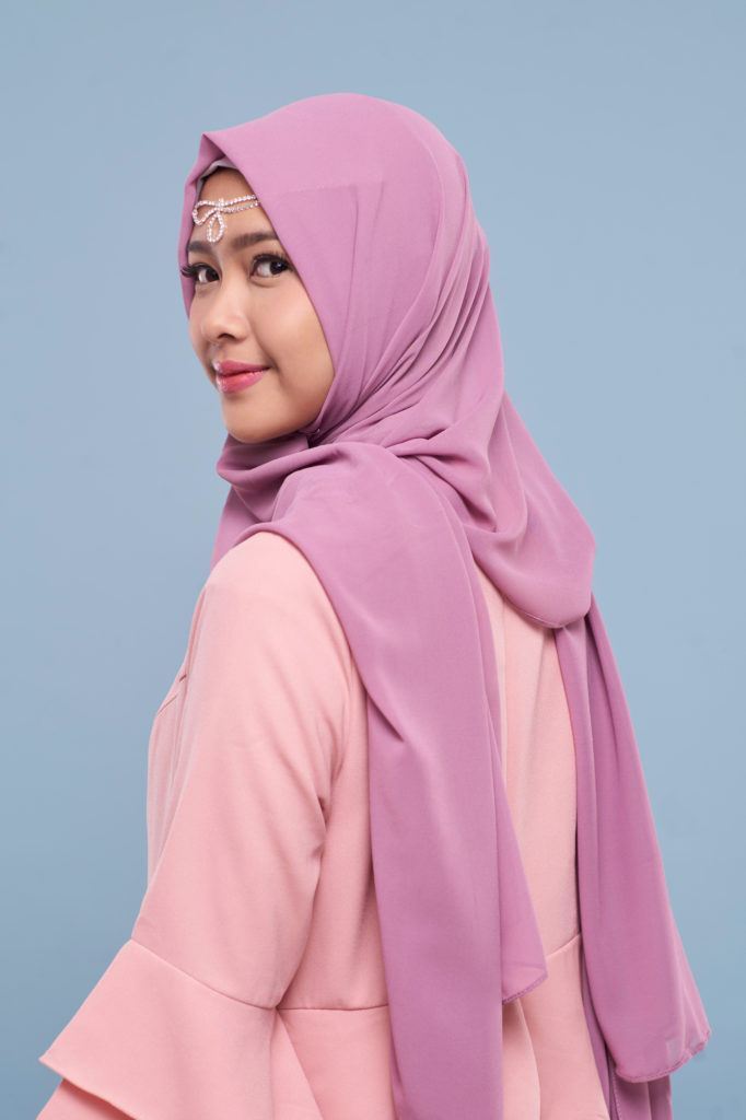 Wanita asia menggunakan hijab warna ungu dan baju warna pink.