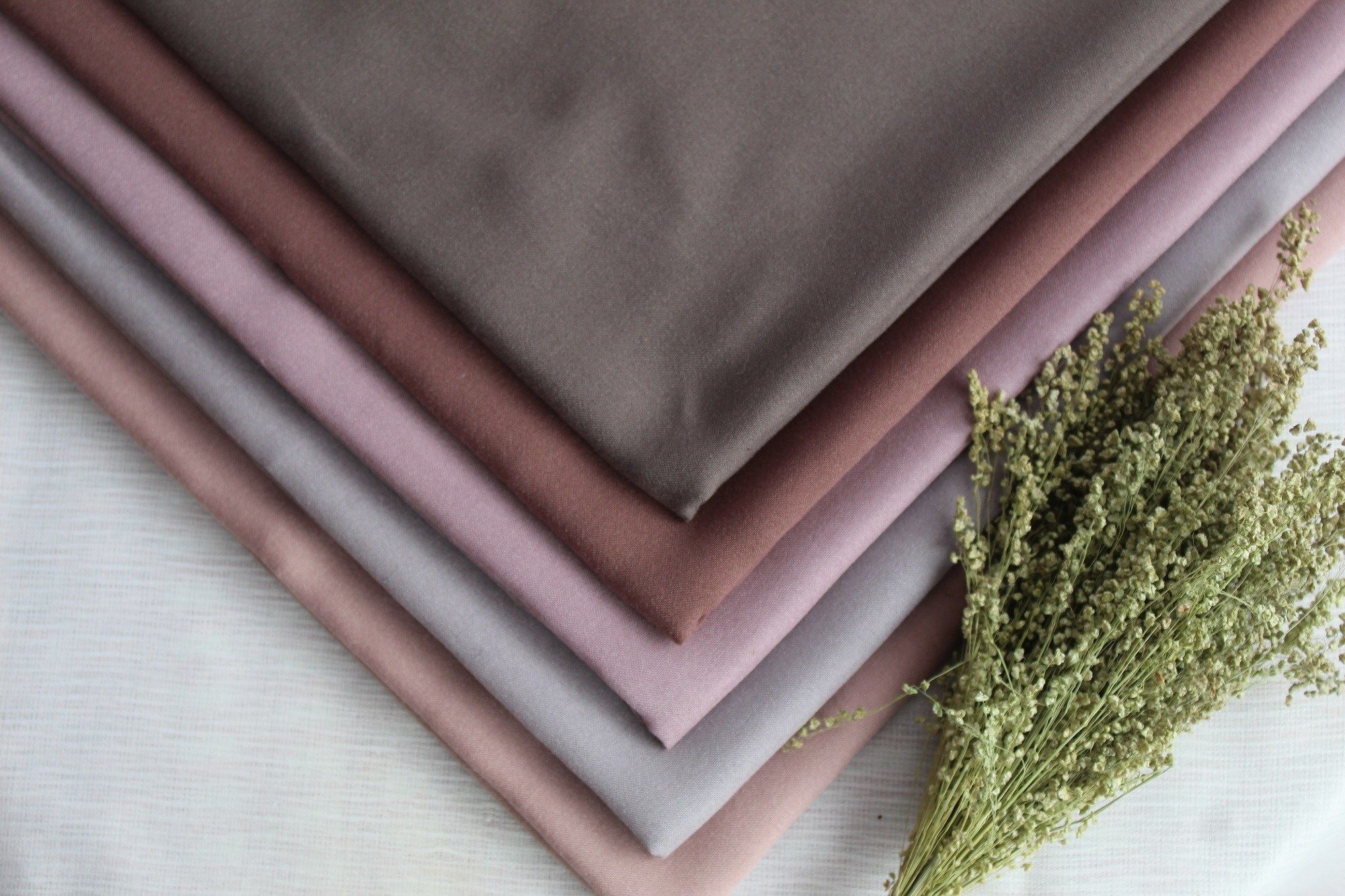 Beragam bahan dan warna hijab yang dilipat dan tersusun rapi.