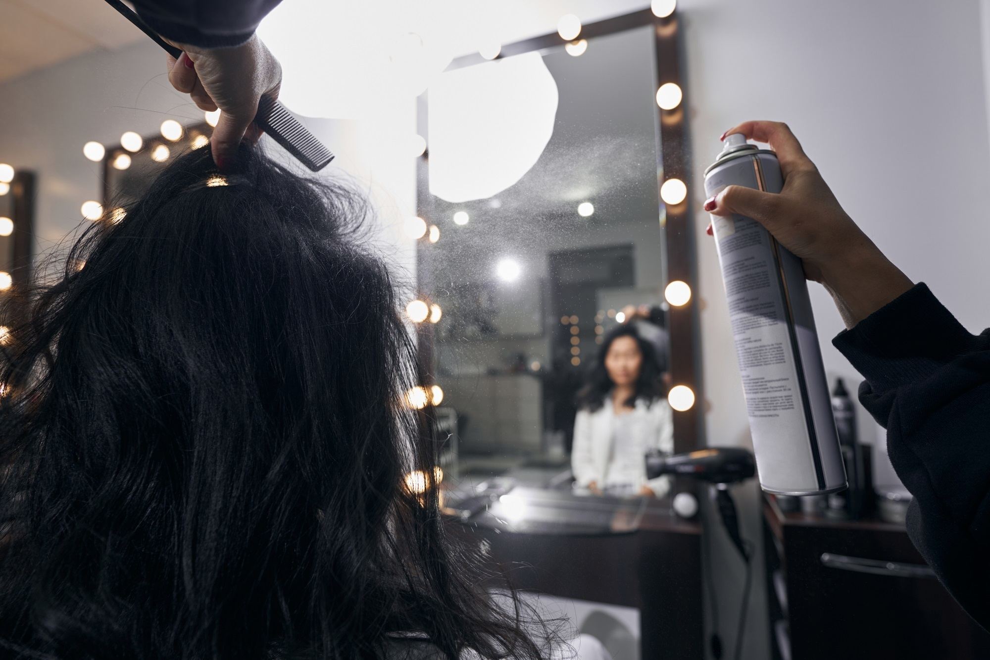 Seorang hairstylist sedang menyemprotkan hair spray ke rambut.