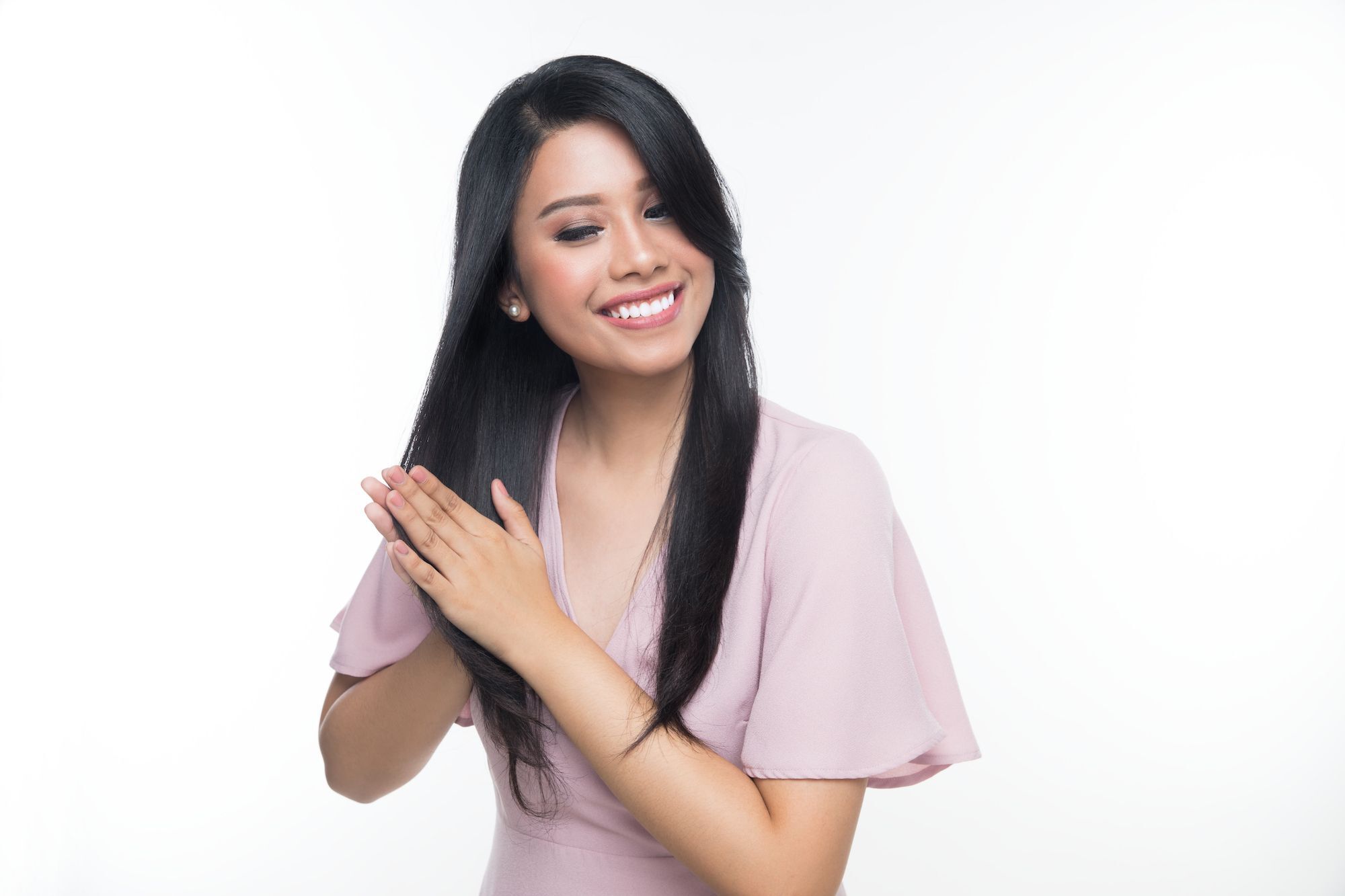 Wanita Asia berambut panjang lurus mengusapkan vitamin pada ujung rambut.