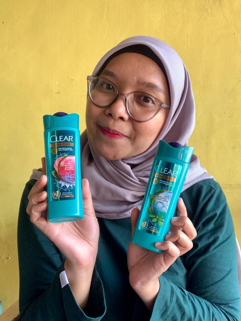 Foto wanita Asia berhijab sedang memegang dua shampoo clear hijab