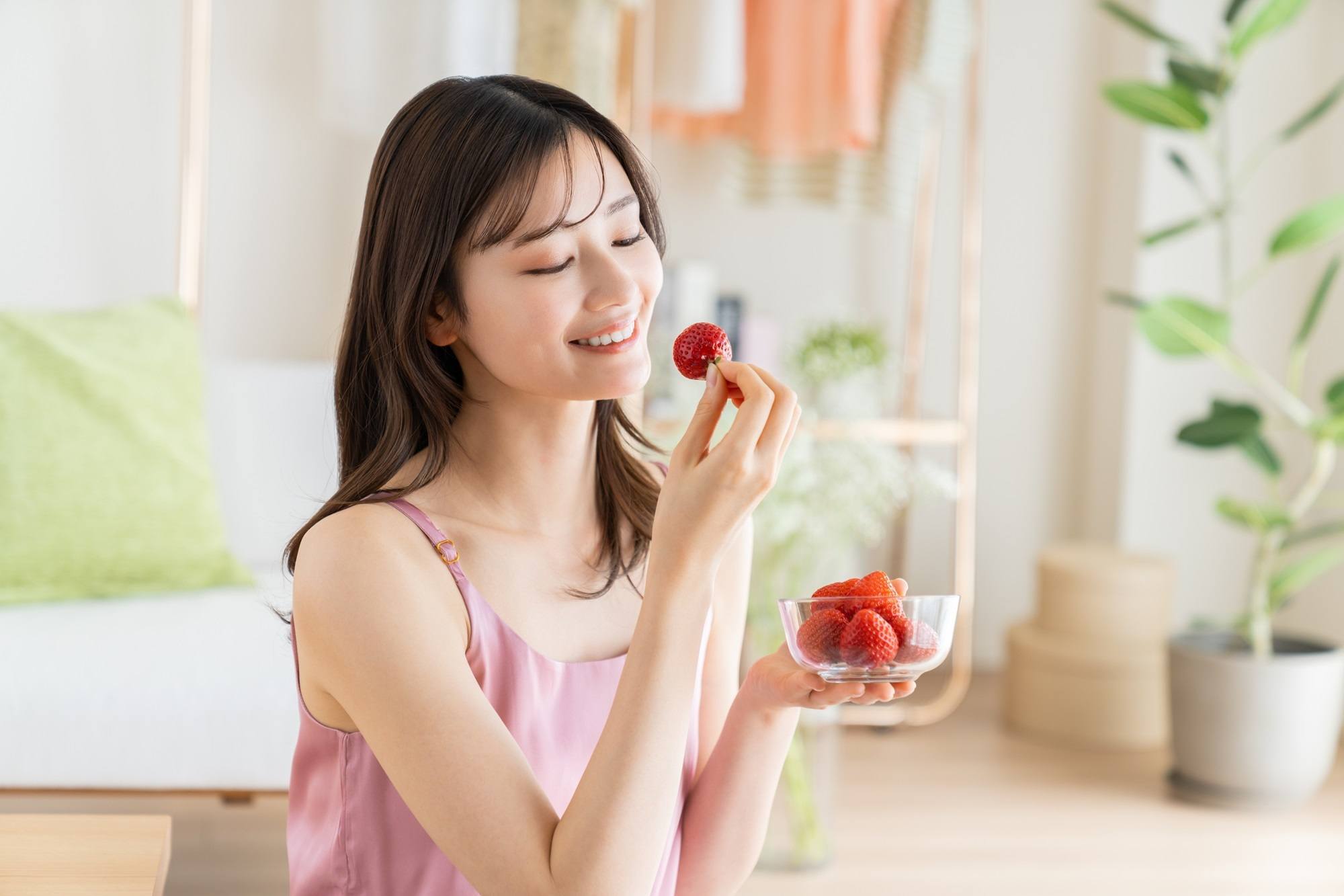 Wanita Asia dengan memegang buah strawberry sambil tersenyum.