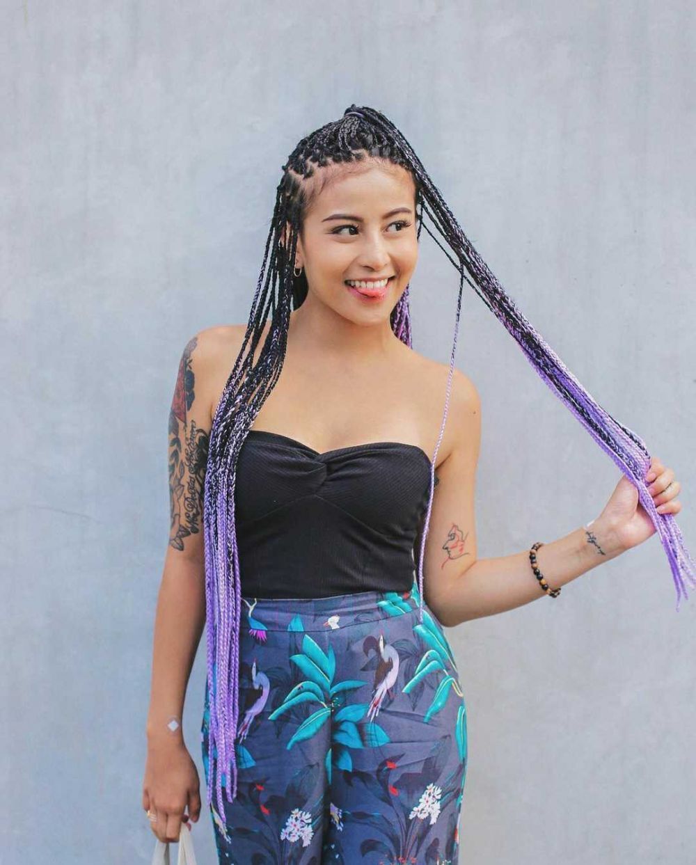Influencer Karin Novilda dengan gaya rambut cornrow warna ungu yang ditata kuncir setengah.