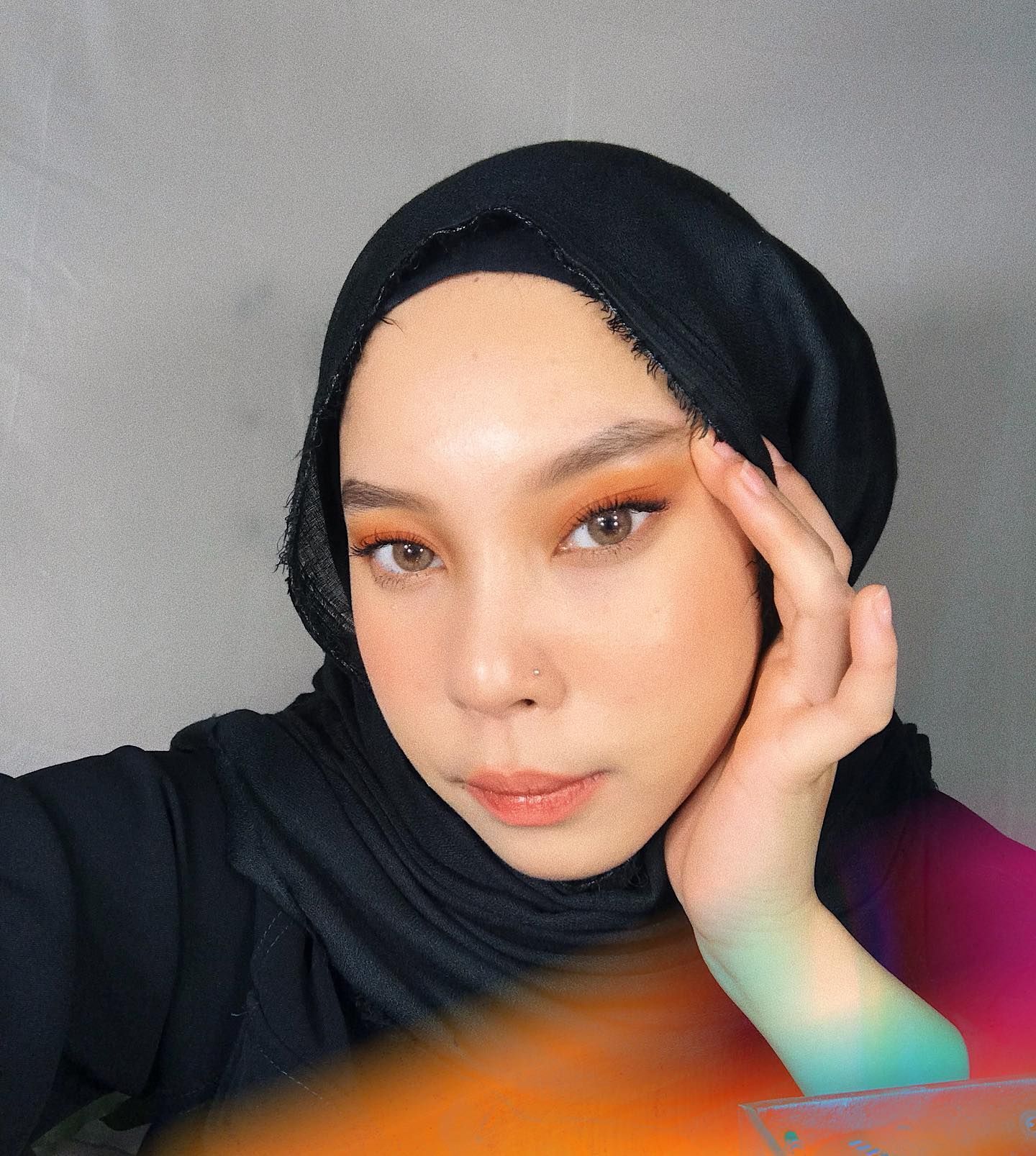 Wanita Asia dengan hijab warna hitam dan make up bernuansa peach.