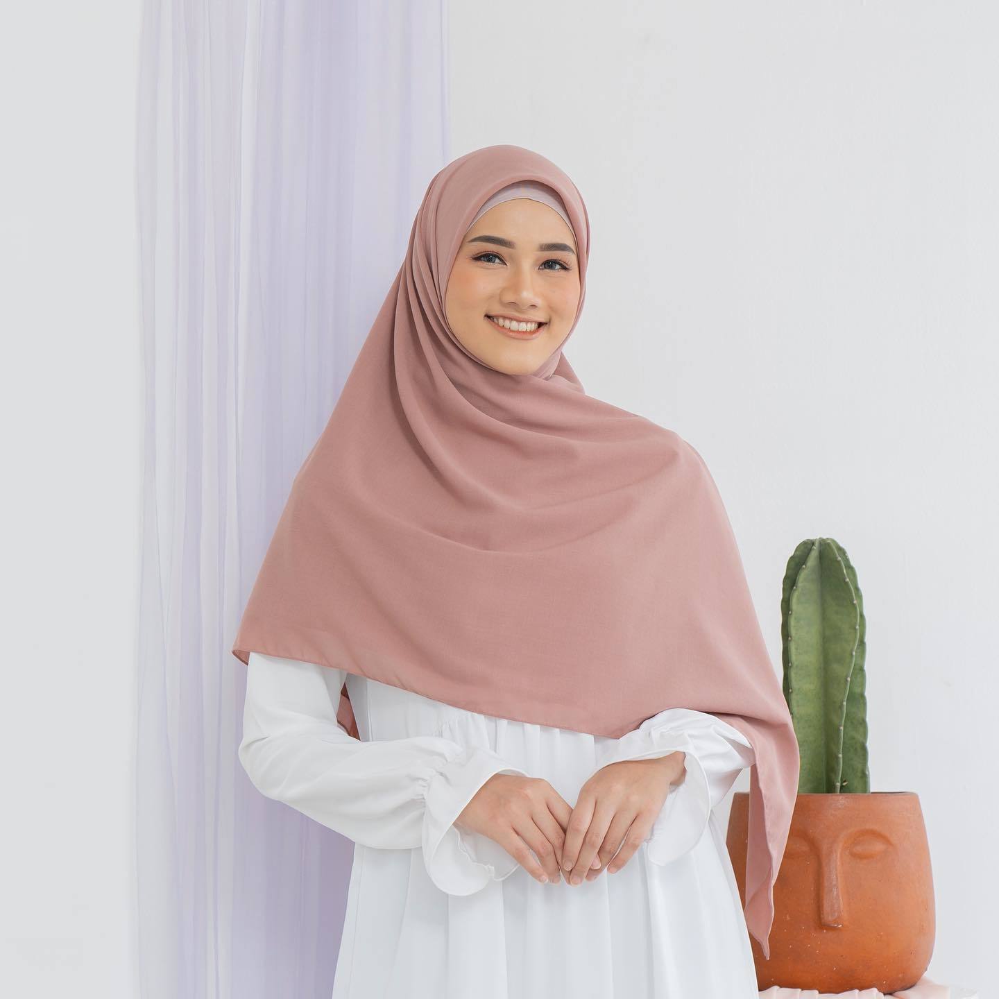 Wanita Indonesia mengenakan hijab syar'i menutup dada warna dusty pink.