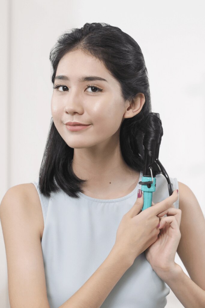 wanita asia sedang mengeriting rambut menggunakan catokan curling iron
