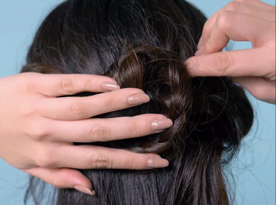 Wanita memasang jepit pada gulungan kepangan rambut.