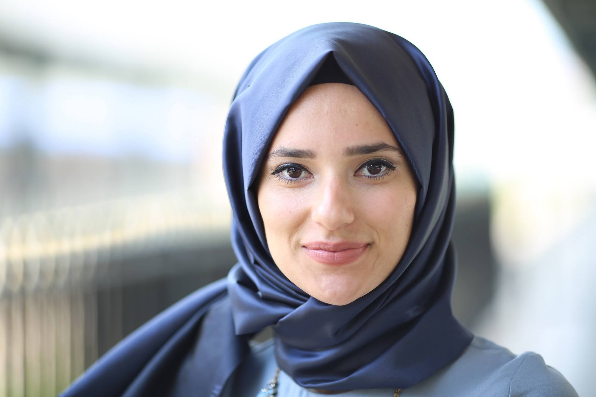 Wanita Turki memakai hijab satin biru dongker dan tersenyum.