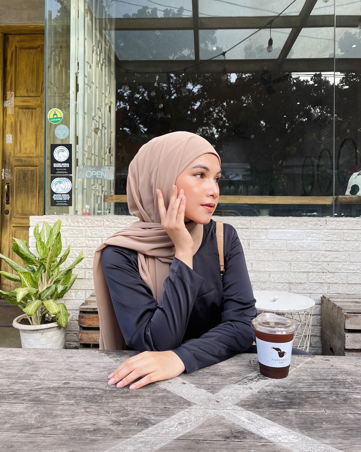 Wanita Indonesia mengenakan hijab pashmina instan warna cokelat muda.